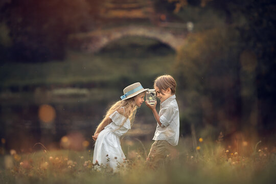 Beautiful long-haired girl and boy are looking at butterflies in the jar in summer park. Image with selective focus and toning