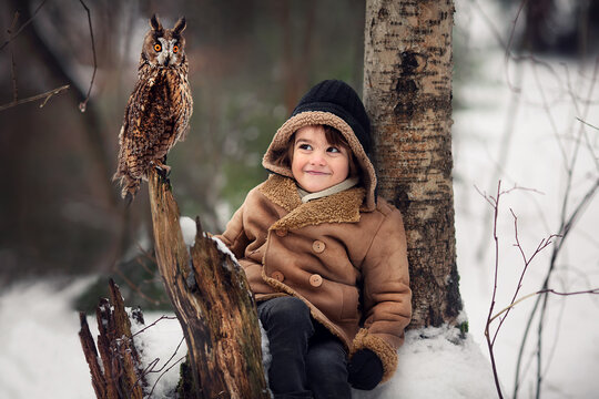 Little boy is meeting an owl in Russian forest in winter. Image with selective focus and toning