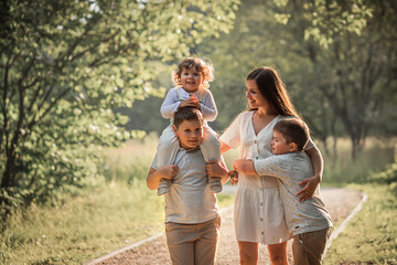 Fototapeta premium Family portrait with young beautiful mother with her three sons in a park. Image with selective focus and toning