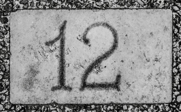 Close Up Outdoor View Of Number Twelve 12 Written In White On A Black And White Square Plate. Numerical Sign Fixed At A House Exterior Wall To Indicate The Address In Street. Vintage Design Image