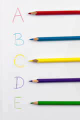 Learning colors and letters with color pencils on white paper. Selective focus.