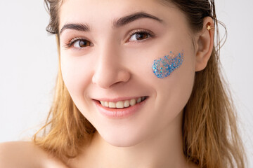 Facial care. Skin peeling cosmetic product. Beauty hygiene. Portrait of happy woman with nude makeup blue beads gel scrub cleanser stroke on flawless face cheek isolated on white background.
