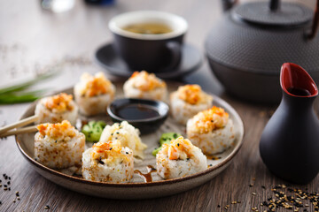 Baked sushi maki rolls with prawns and crab on a plate with chopsticks, soy sauce, wasabi and ginger. Japanese traditional fish food closeup served for lunch in modern gourmet restaurant