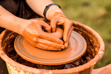 Hands of man in shape of heart in clay on pottery wheel mold vase. Potter works in pottery workshop with clay. 