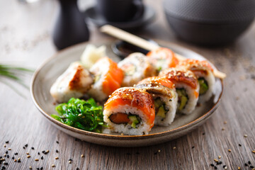 Sushi maki rolls with salmon, eel, avocado, cucumber on a plate with chopsticks, soy sauce, wasabi and ginger. Japanese traditional fish food closeup served for lunch in modern gourmet restaurant