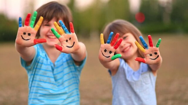 Two funny sisters smile and waving painted hands outside in summer. Focus on hands