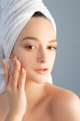 Facial skincare. Acne treatment. Health beauty wellness. Portrait of woman with nude makeup bare shoulders white towel on head touching flawless face skin after cleansing isolated on gray background.