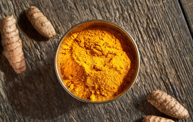 A bowl of turmeric powder, with fresh turmeric root in the background