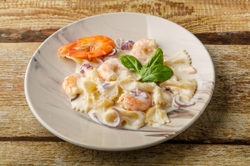 Farfalle pasta with shrimps in a creamy sauce on a gray plate on a wooden table.