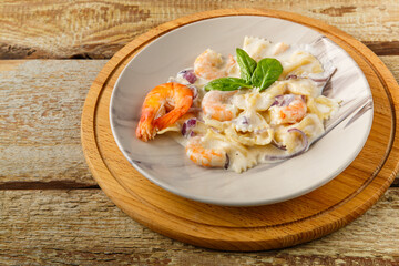 Pasta with shrimps in a creamy sauce on a gray plate on a wooden table on a stand.