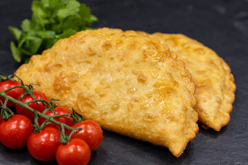 Chebureks on a black background. Served with coriander and cherry tomatoes. Caucasian cuisine.