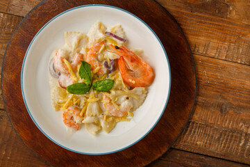 Pasta with shrimps in a creamy sauce, decorated with spinach on a gray plate on a wooden table on a stand.