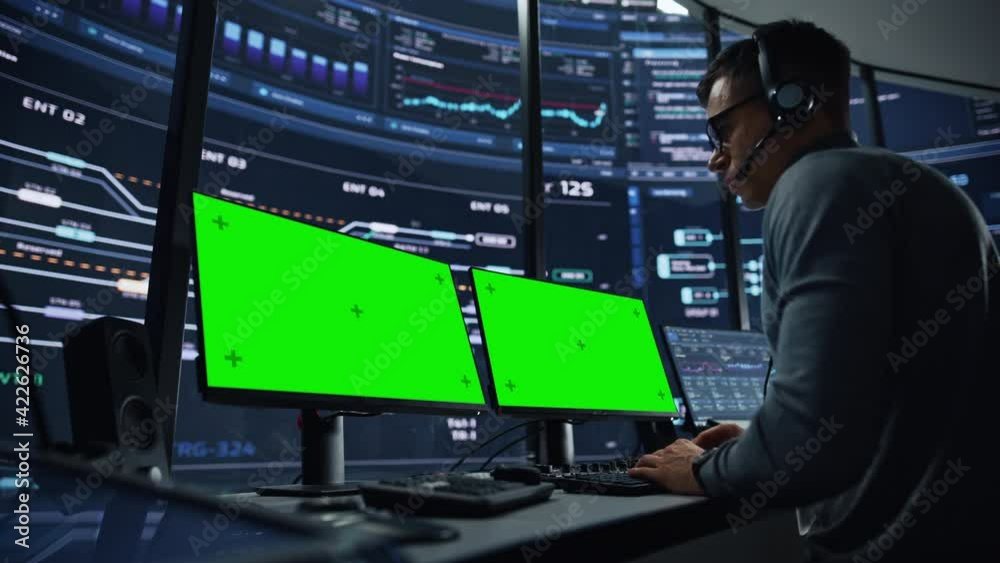Poster Professional IT Technical Support Specialist and Software Developer Working on Computer with Green Screen Mock Up Display in Monitoring Control Room with Digital Screens. Employee Wears Headphones.