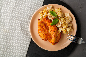 Baked chicken breast with salad on a plate decorated with spinach next to a fork on a concrete background on a gray napkin.
