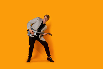 Fototapeta na wymiar Stylish and cool guy in a suit and with a game guitar on a yellow background, playing and dancing,