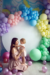 Fototapeta na wymiar mom and daughter in pink dresses sit on a white background with colorful balloons