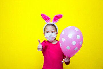 Obraz na płótnie Canvas A girl in a pink T-shirt and rabbit ears on a yellow background in her hands holds a balloon and shows a finger class, cool, place for advertising. 