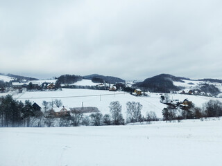 Wide angle shot of small polish town covered with white snow and a framed houses against small mountains in southern Poland located the Lesser Poland Voivodeship. Winter scenery of Central Europe.