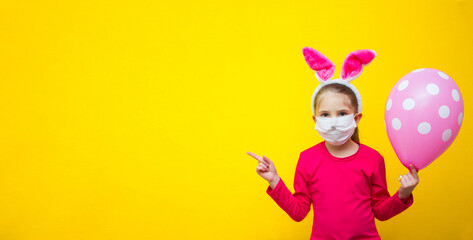 A girl in a pink T-shirt and rabbit ears on a yellow background in her hands holds a balloon and shows a finger class, cool, place for advertising. 