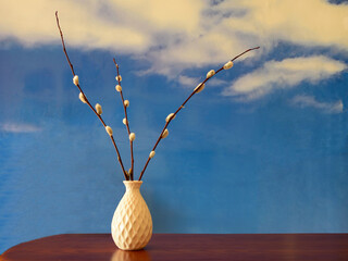 Willow spring branches with buds in a vase on the table against the background of the blue sky. Orthodox Easter 
