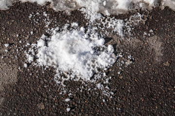 A crushed snowball with an imprint of the sole on the asphalt. Melting snow in spring