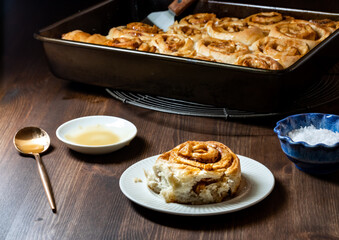Close up of a homemade cinnamon bun topped with caramel sauce with the rest of the buns in a baking...