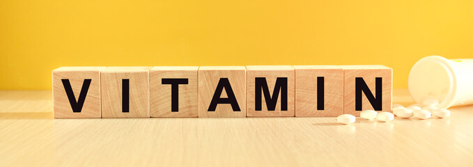 inscription VITAMIN on wooden cubes on a yellow background with pills