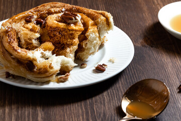 Close up of a homemade cinnamon bun topped with caramel sauce and crushed pecans, broken open to show the inner spiral