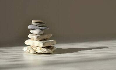 Balance pyramid stones on grey background, sunlight and shadows. Copy space