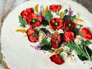 Fototapeta na wymiar White cream cake decorated with buttercream flowers, Poppies, chamomile, cornflowers, spikelets of wheat, on gray background. Selective focus, closeup view, top view, retro.