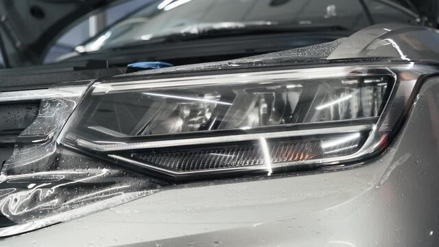 Detailer worker smoothes PPF or Paint Protection Film on Car Headlight with working tool. Polymer protective outer coating, close up.