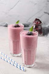 Two servings of homemade smoothies with frozen blackberries in tall glasses on gray background, Diet and weight loss control concept