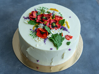 White cream cake decorated with buttercream flowers, Poppies, chamomile, cornflowers, spikelets of wheat, on gray background. Selective focus, closeup view, top view, retro.