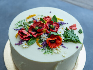 White cream cake decorated with buttercream flowers, Poppies, chamomile, cornflowers, spikelets of wheat, on gray background. Selective focus, closeup view, top view, retro.