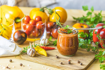 Homemade DIY natural canned hot plum sauce chutney with chilli or tkemali in glass jar standing on wooden table with ingredients.