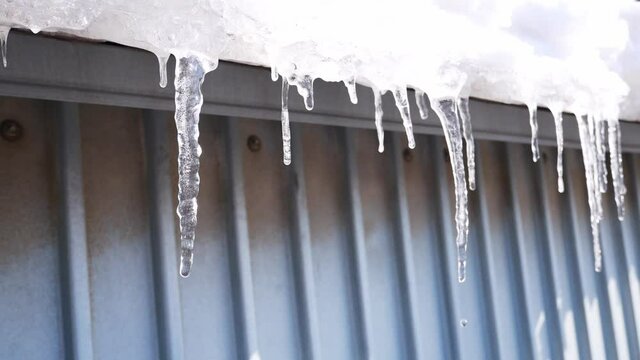 Icicles melt and drip from the roof, spring day, close-up, hand-held shooting