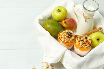 A wooden tray with fruit, a jug of milk and homemade yogurt with granola. On a light wooden background, horizontally with space