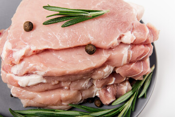 raw pork meat on the plate with rosemary, salt and pepper. flat lay on the white background. close-up view