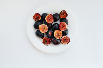 Ripe and sweet figs cut and arranged in a plate on a white background with free space. Fruits and vegetarianism