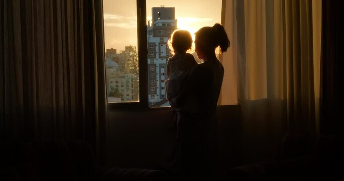 Family watch sunset. Woman stands with girl near the window and they both enjoy sunset in the city