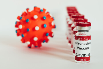 Covid-19 vaccine - coronavirus vaccination bottles. Injection vials in a row beside molecule of coronavirus on white background. Healthcare and medical concept.