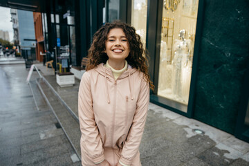 Obraz premium Charming young curly woman with beautiful smile walking the street of the city and turns around at rainy day 
