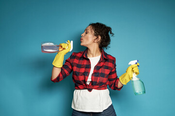 Attractive and playful young Latin American woman, a housewife, holding a cleaning spray in her...