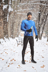 Fit man in running clothes holding a drink bottle on a snowy day outdoors