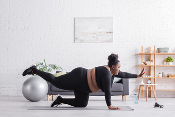 side view of cheerful african american plus size woman in sportswear exercising on fitness mat