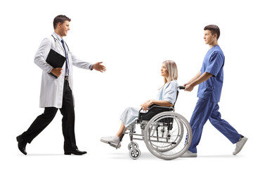 Full length profile shot of a doctor greeting a young woman patient in a wheelchair and a male nurse