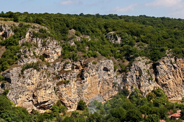 View of the beautiful village of Nisovo, Bulgaria, located below, above and in the high limestone cliffs, protected by magnificent deciduous trees   