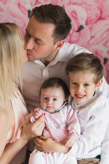 A happy family. Father, mother, son and baby daughter. The father holds the children in his arms and kisses his wife. Exemplary family.