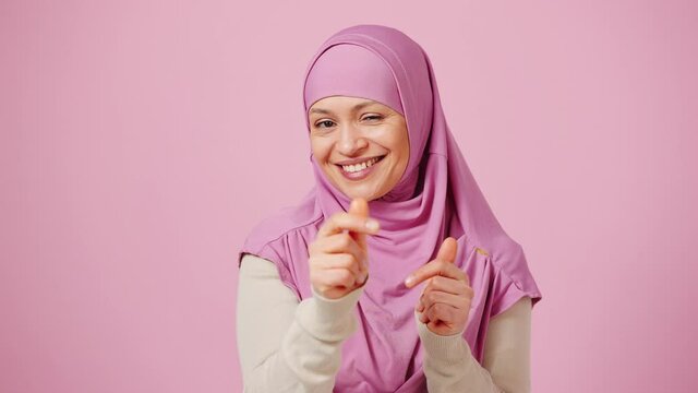 Thoughtful middle aged islamic woman looking at camera with evaluation and pointing gotcha, pink background