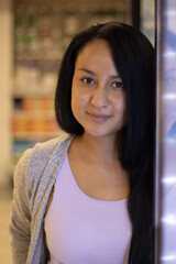 Happy young girl smiling next to some lights in a store with a lead-colored jacket and white blouse
